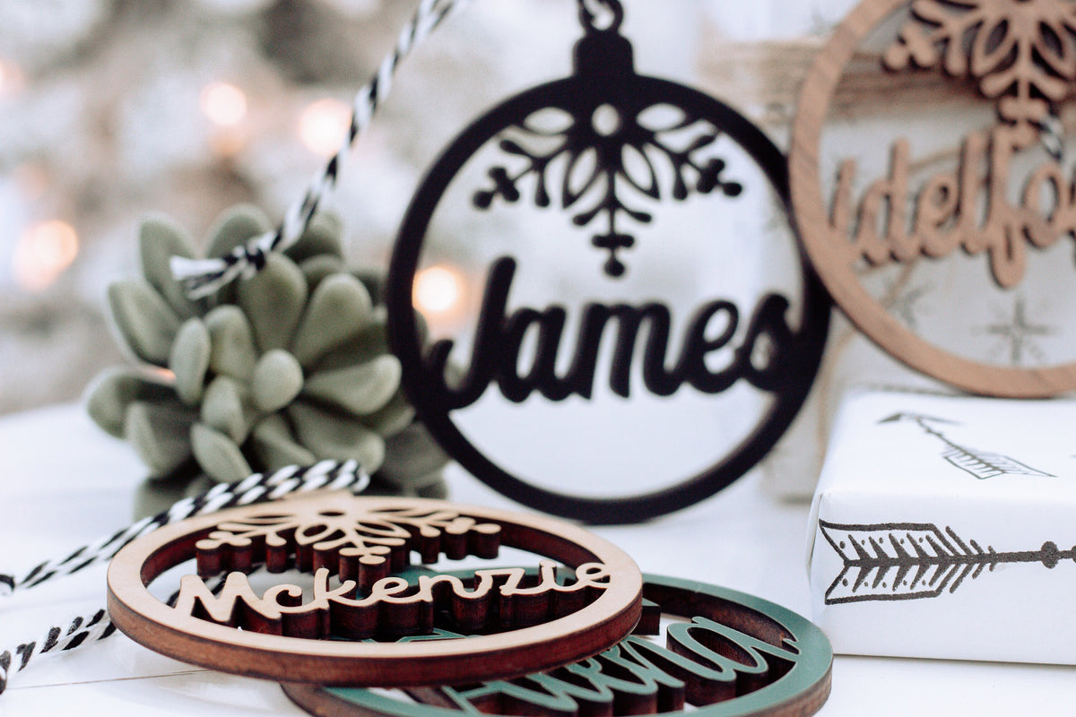Hanging round name ornament with snowflake design, dark text on a light background