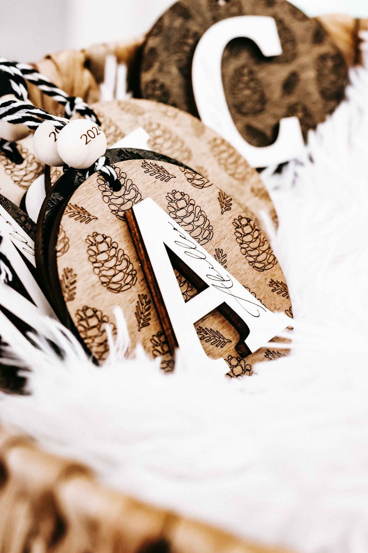 Round engraved pine cone ornament with zebra-striped loop and year 2024 tag, letter A