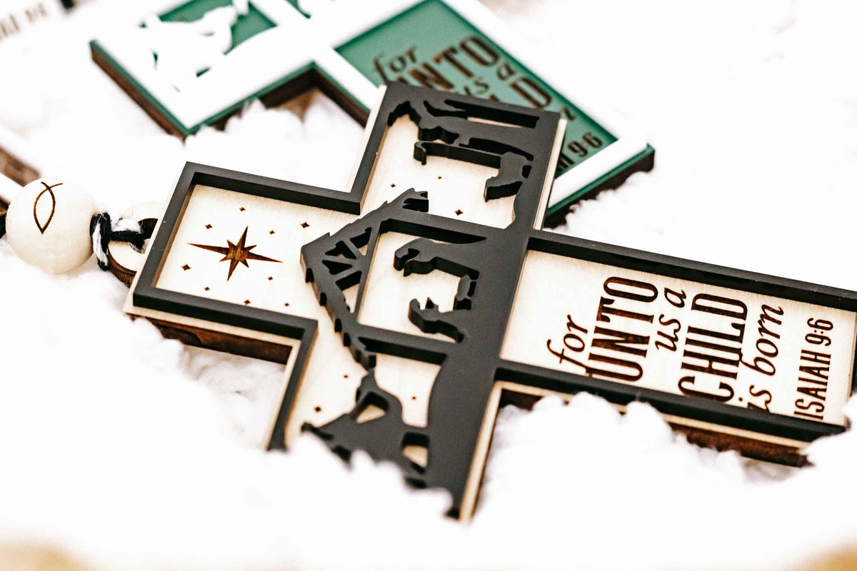 Close-up of black and teal cross nativity ornaments with star and nativity figures
