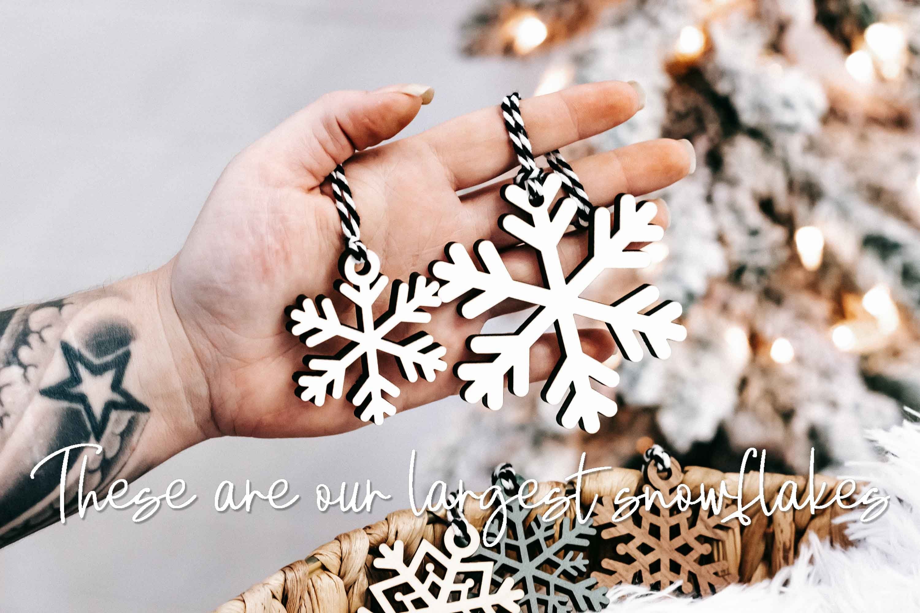 Hand holding wood snowflake ornament: white and dark layered cutout with braided string
