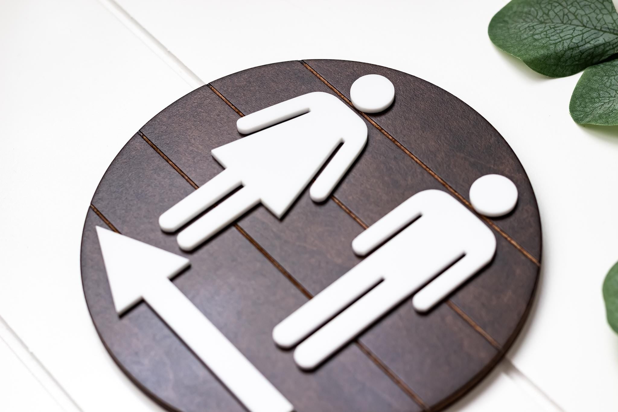 Directional restroom sign with white male icon and left-pointing arrow on dark round backing