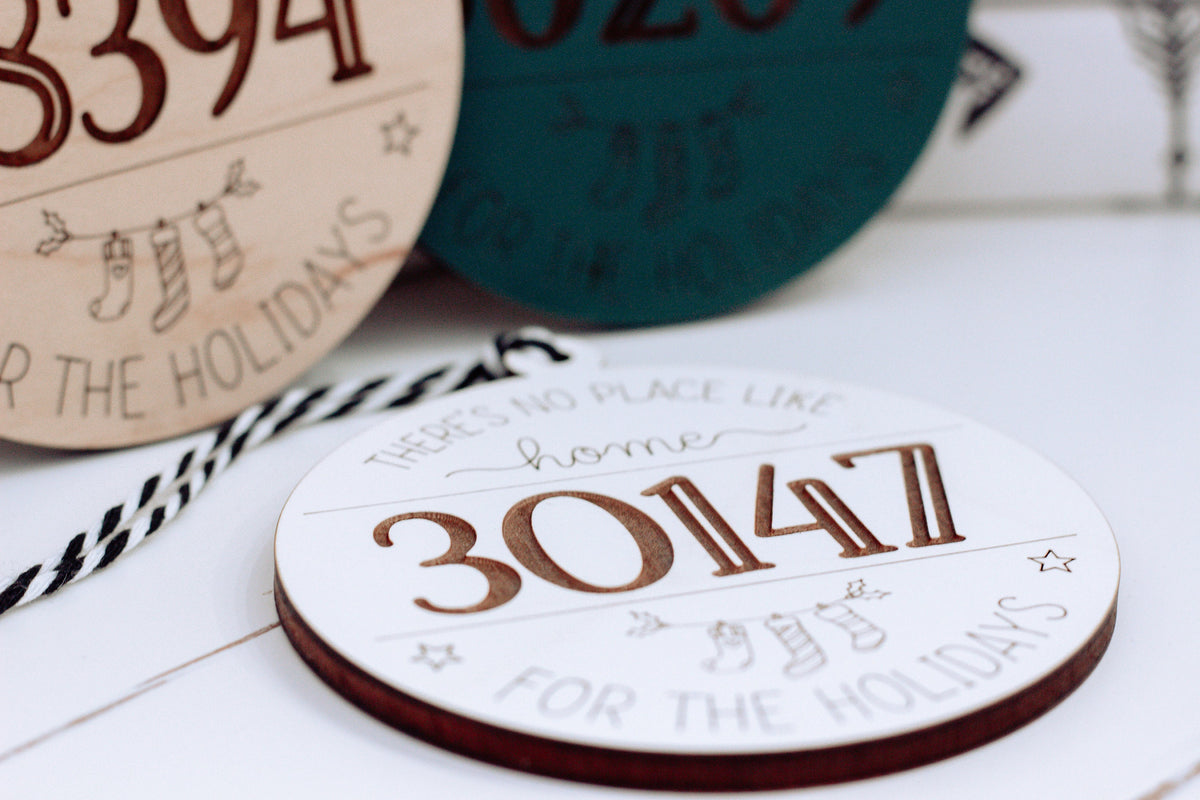Round personalized home holiday ornament with “30114” in orange on white wood.