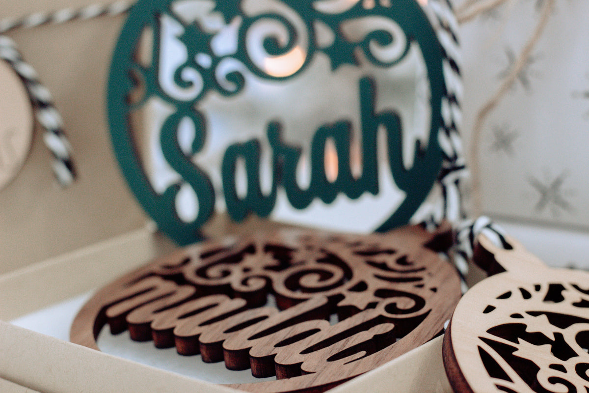 Close-up of green laser-cut name ornament with scrollwork in gift box