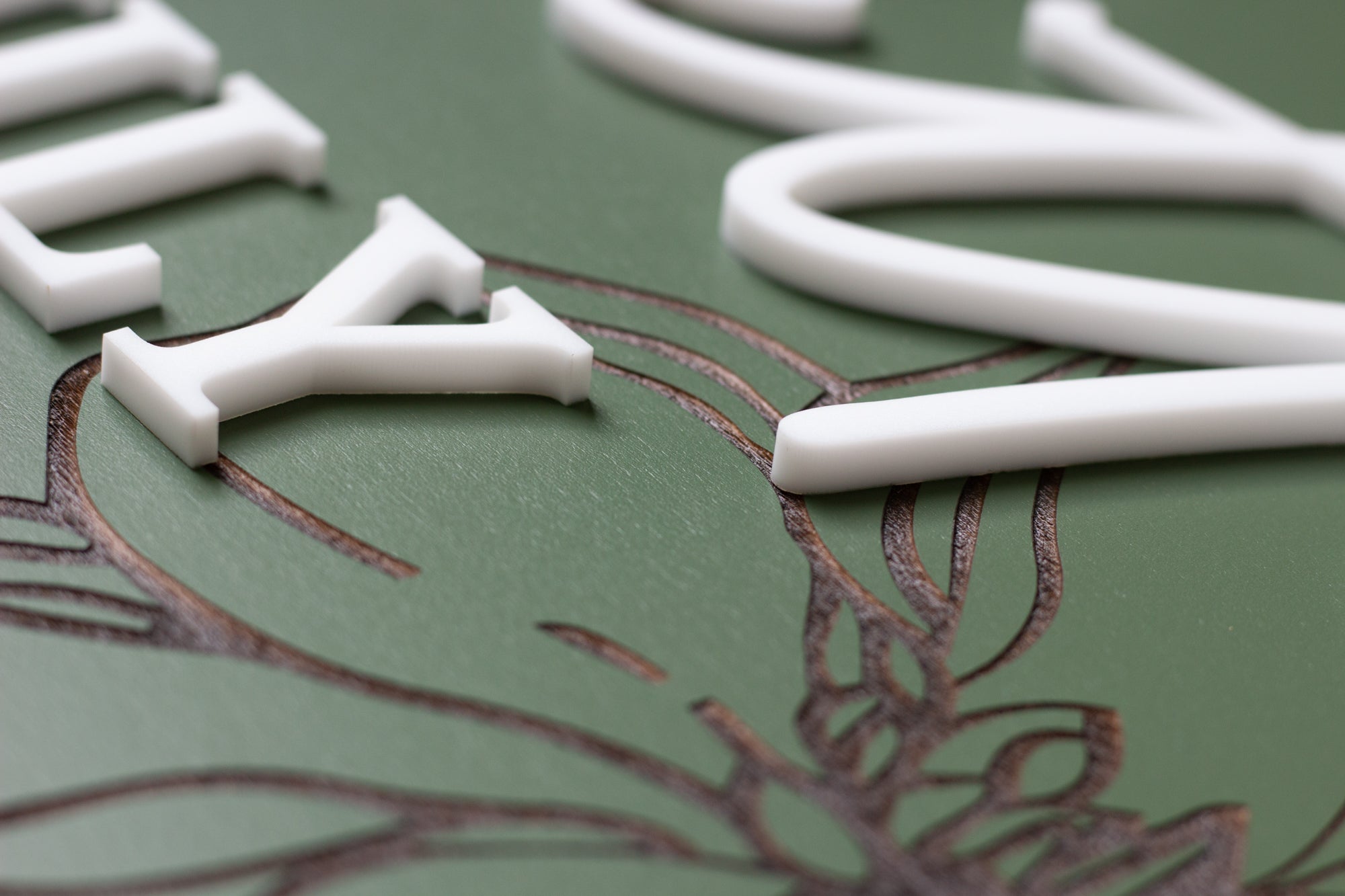 Close-up of green rectangle sign with white letter shapes and floral engraving detail