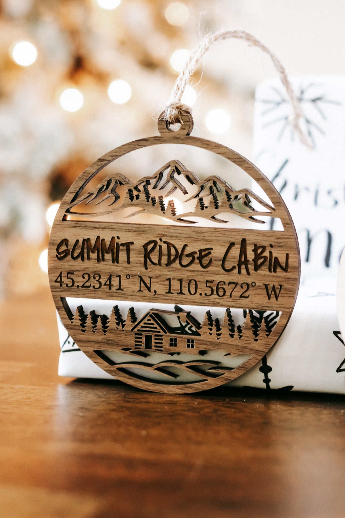 Engraved circular wood ornament reading “SUMMIT RIDGE CABIN” with coordinates, hanging from twine