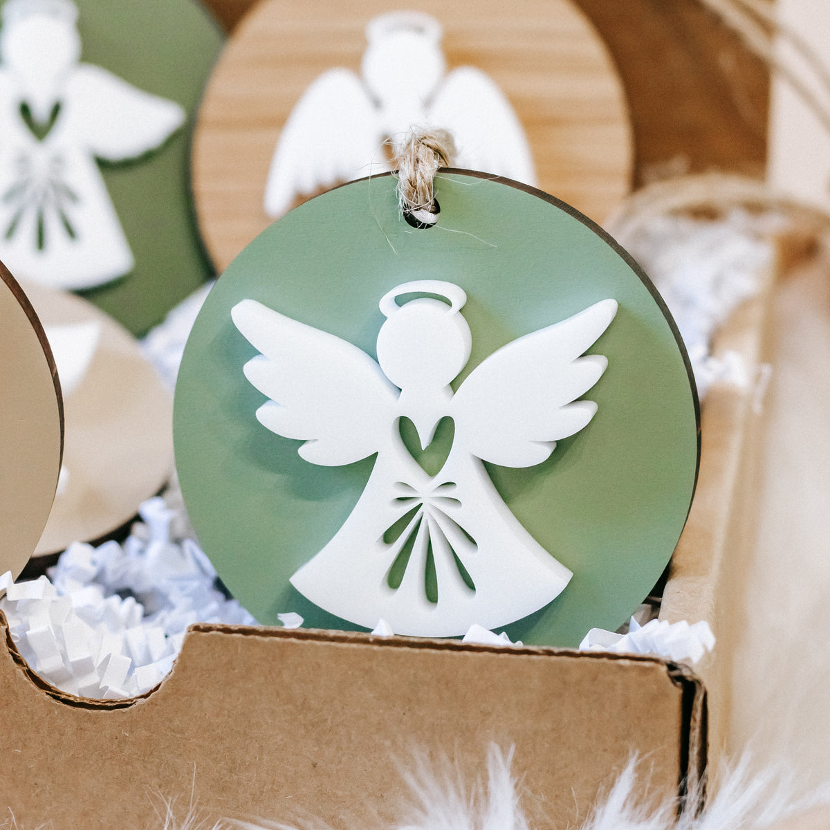 Green round angel ornament close-up with white wings, heart-shaped detail, twine loop