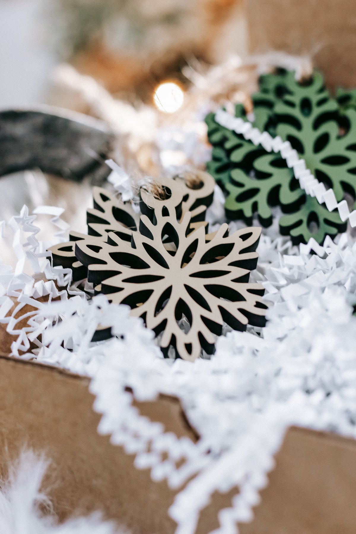 Green and natural wood snowflake ornament with twine loop, surrounded by paper shreds