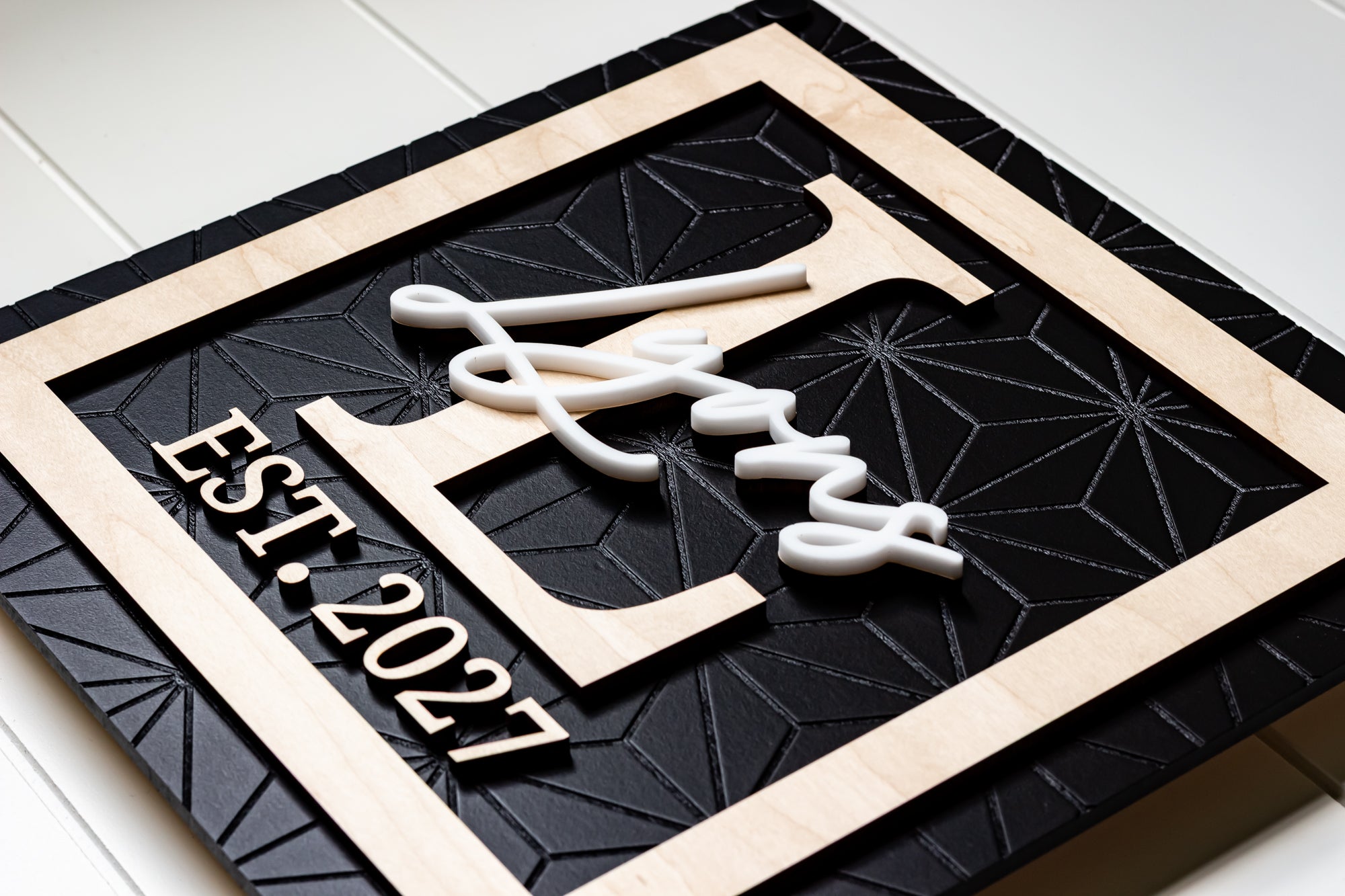 Rectangle family name sign with white cursive letters, dark geometric board, light wood frame
