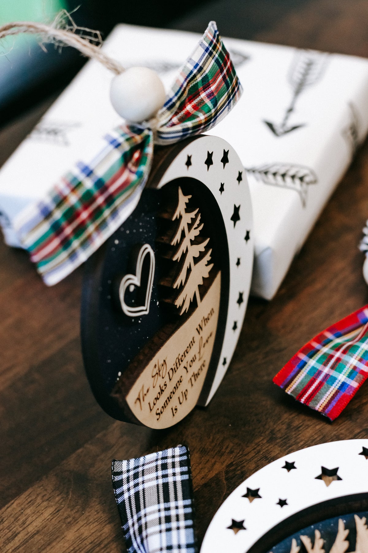 Side view round memorial ornament with plaid bow, heart and tree graphic, hanging loop.