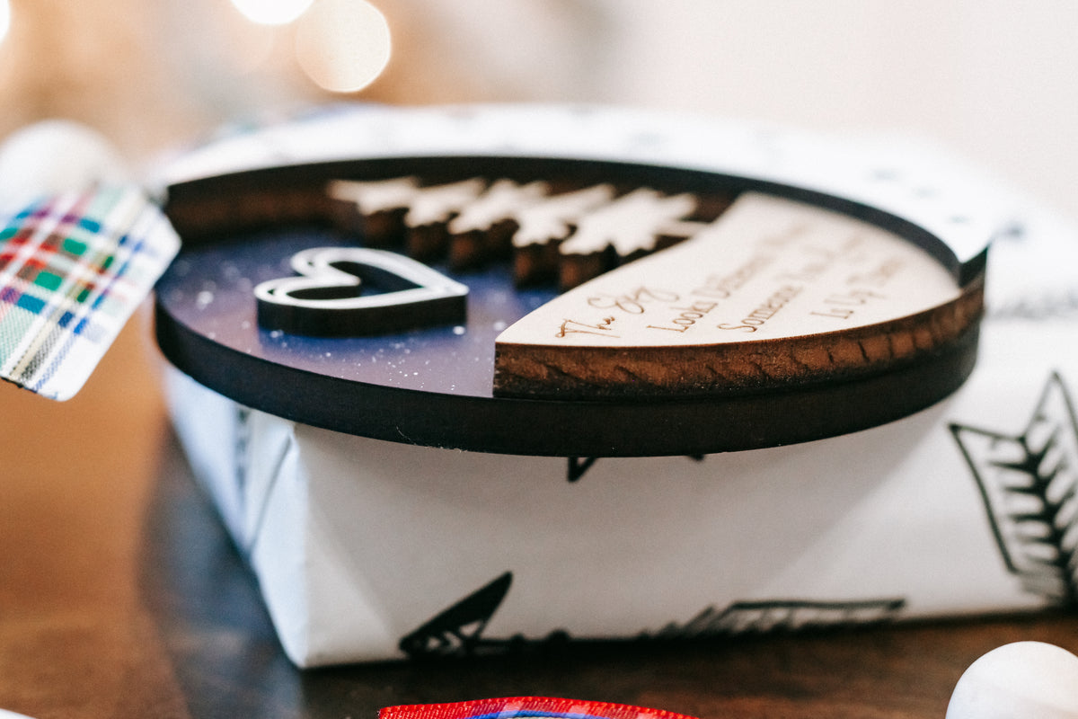 Gift-wrapped box with round memorial ornament disc, dark rim and printed tree design.