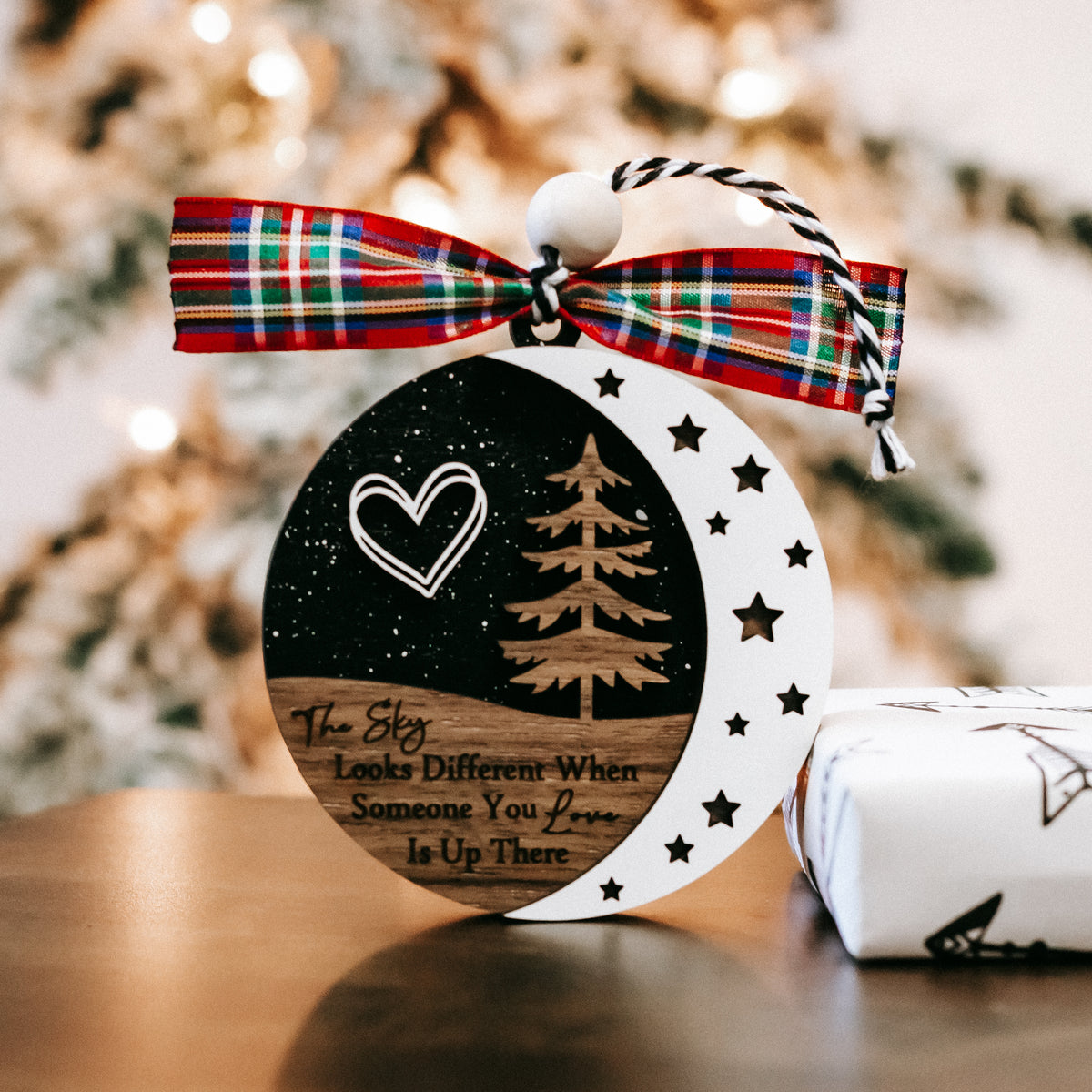 Round memorial Christmas ornament, black-and-white sky design, plaid bow, hanging loop.