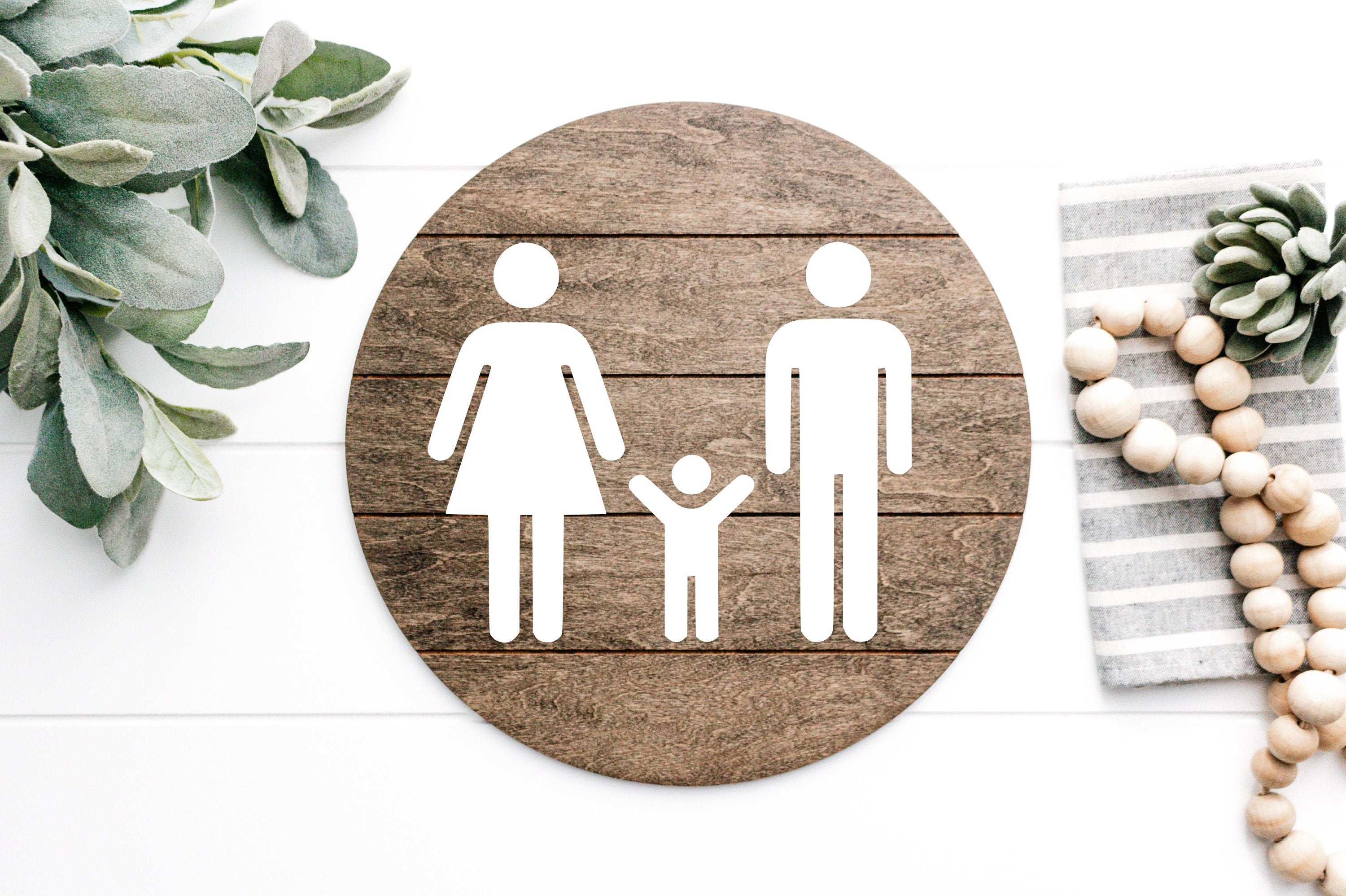 Round wood restroom sign with raised female, male, and child icons