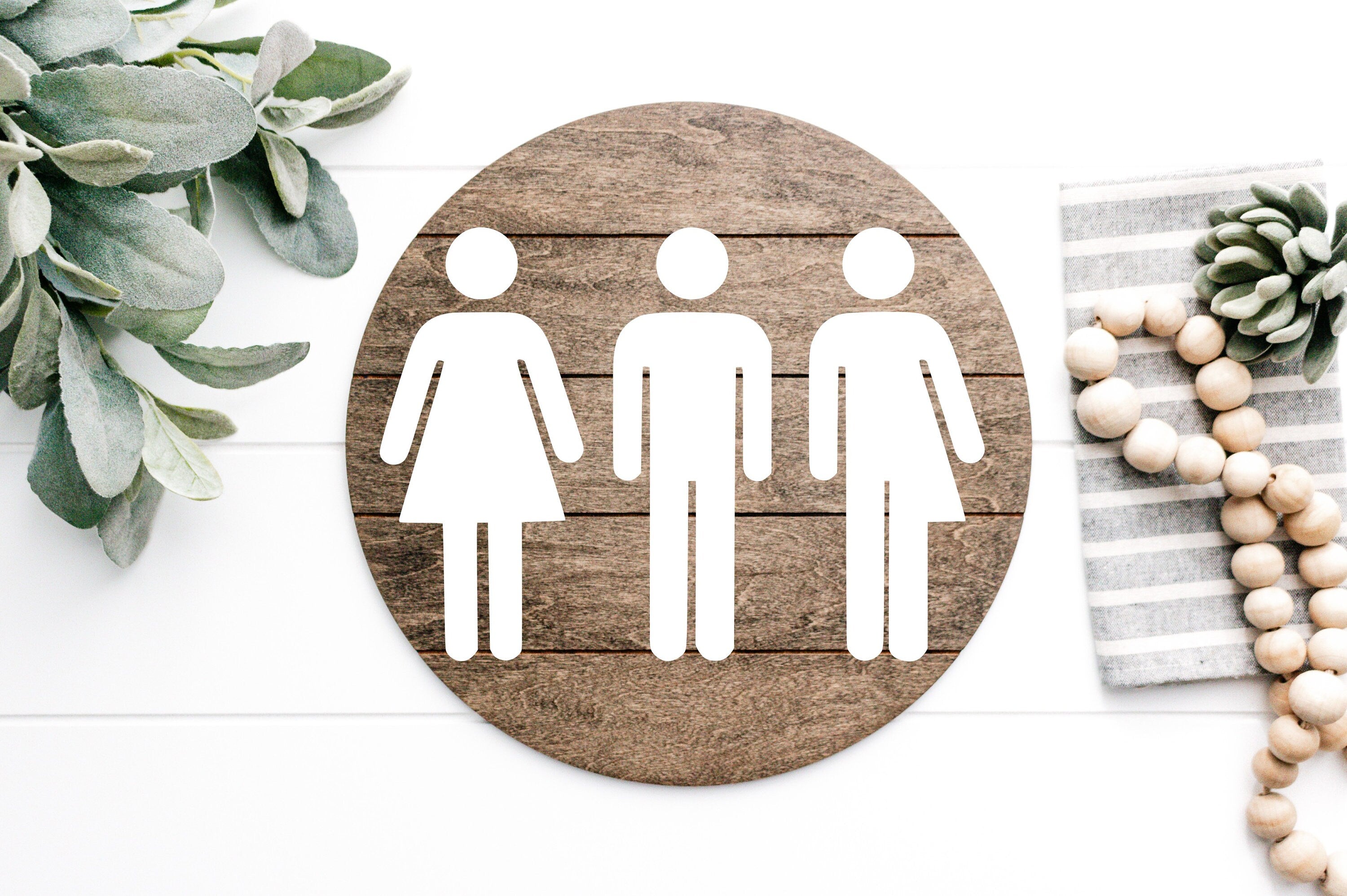Round wood-look restroom sign with white unisex toilet icons for women, men, and all-gender