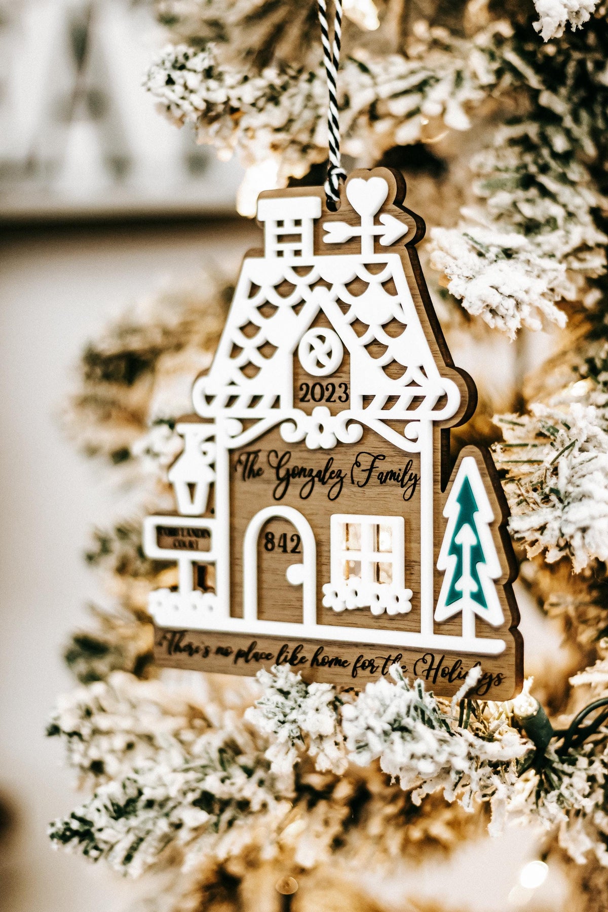 Wood gingerbread house ornament hanging on snowy branches with “2023” and teal tree