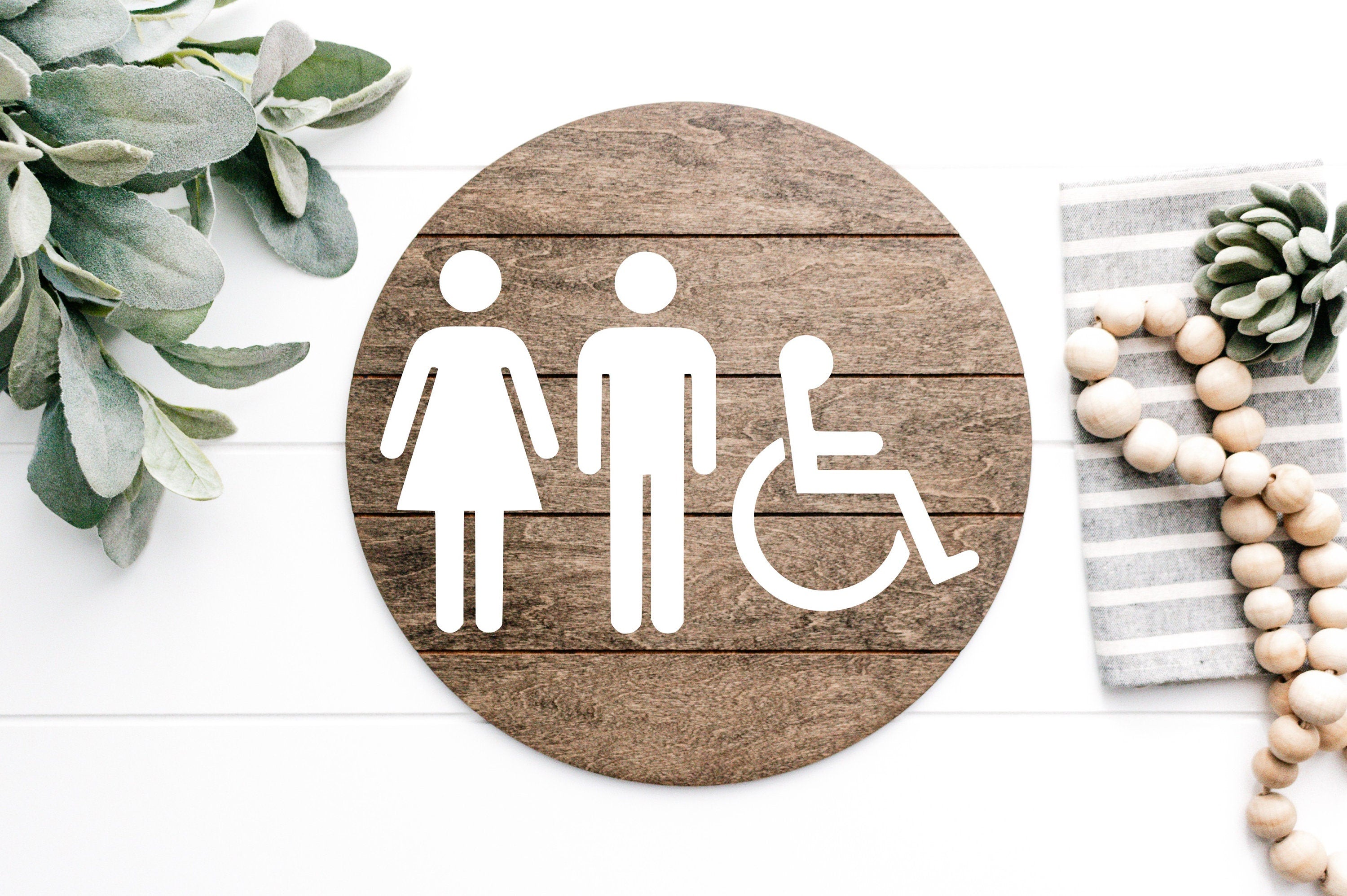 Round 3D restroom accessibility sign with white male, female, and wheelchair icons