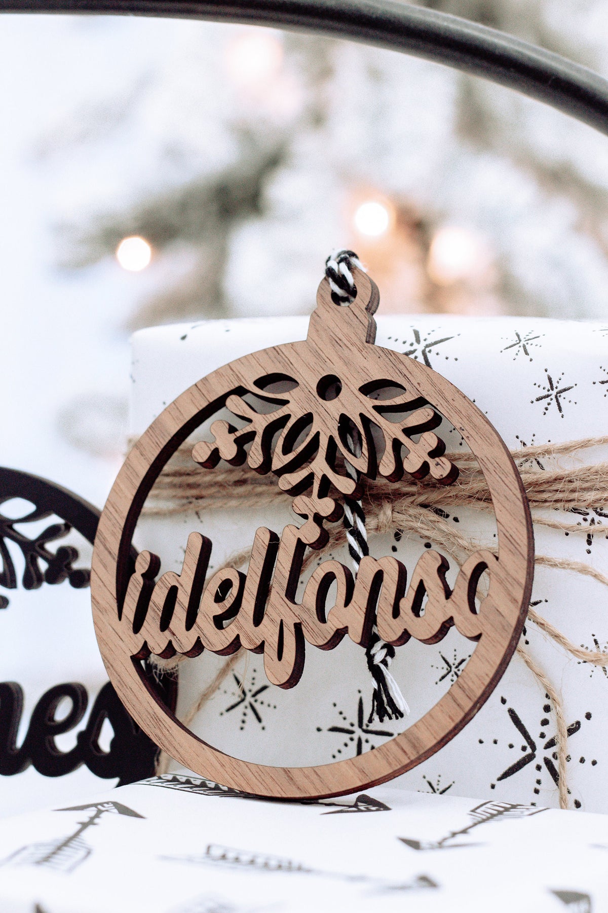 Wooden round snowflake name ornament hanging from a black rope, light wood face