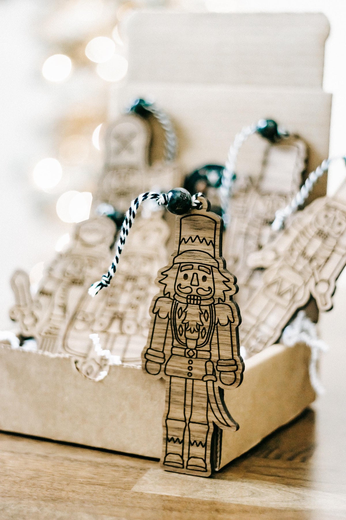 Engraved wooden nutcracker ornament with dark bead hanger standing in a gift box