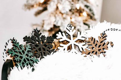 Wooden snowflake ornaments in dark, natural wood, and white tones with hanging loop tops