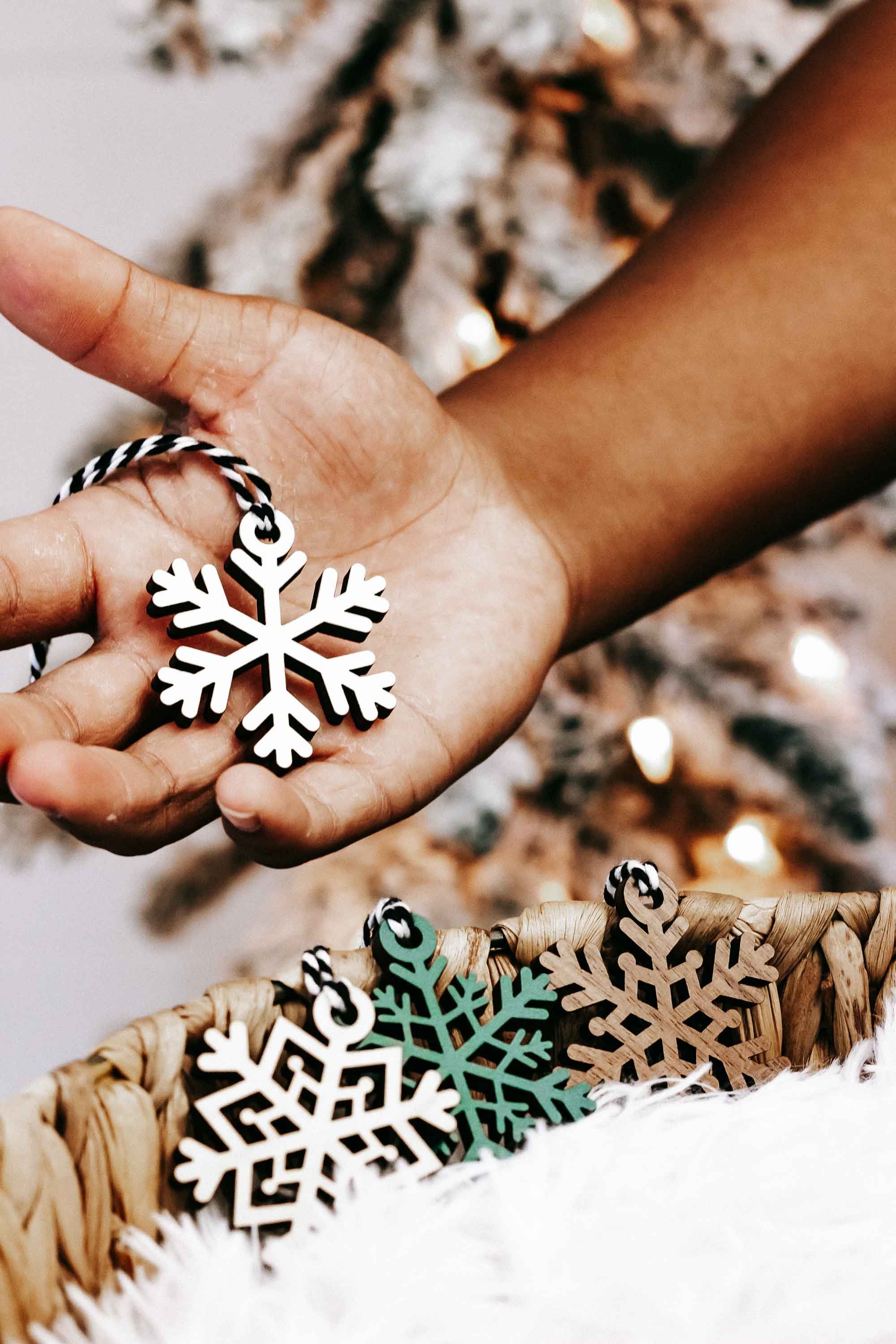 Hand holding a wooden snowflake ornament; twine-hung ornaments with teal, tan, and white