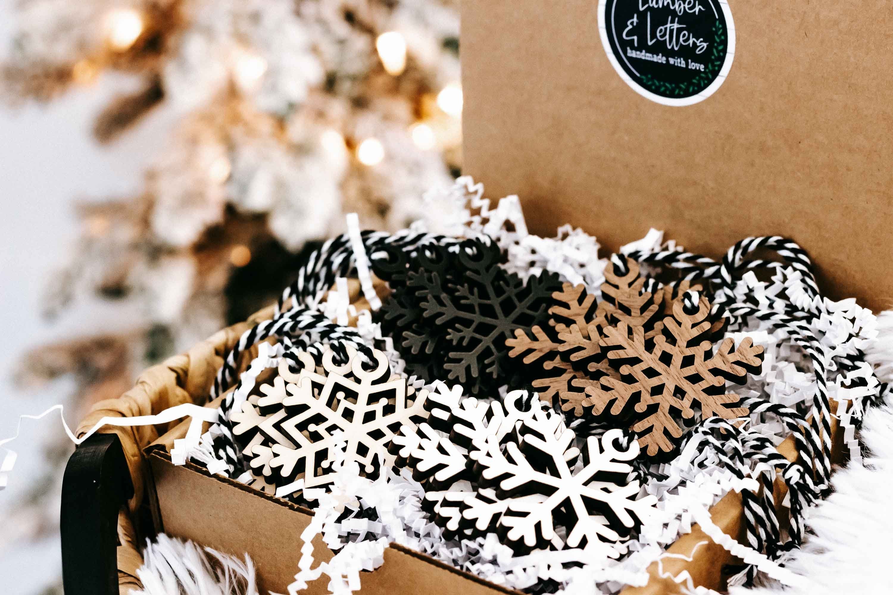 Snowflake wooden ornaments in kraft packaging, layered black and white cutout snowflake shapes