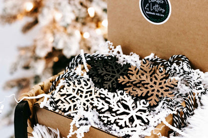 Snowflake wooden ornaments in kraft packaging, layered black and white cutout snowflake shapes