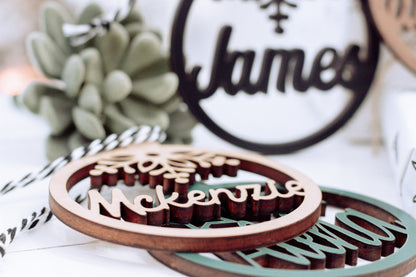 Round dark-edged name ornament with snowflake, plus another engraved ornament nearby