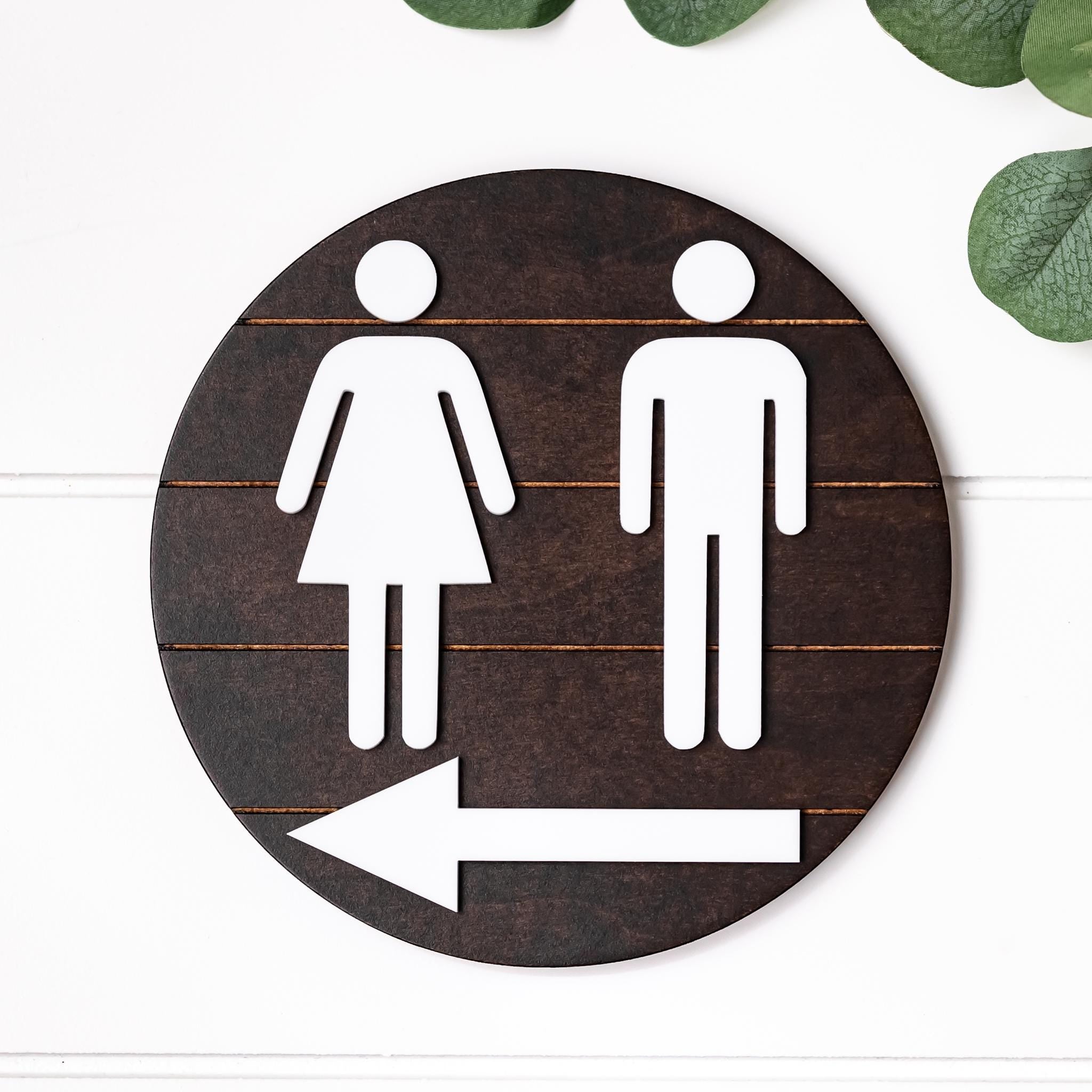 Directional restroom sign with white female icon and left-pointing arrow on dark round backing