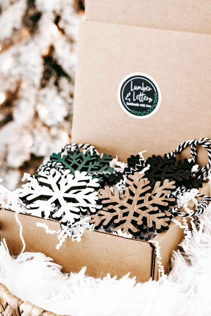 Kraft box with wooden snowflake ornaments in dark, green, and natural wood, string hangers