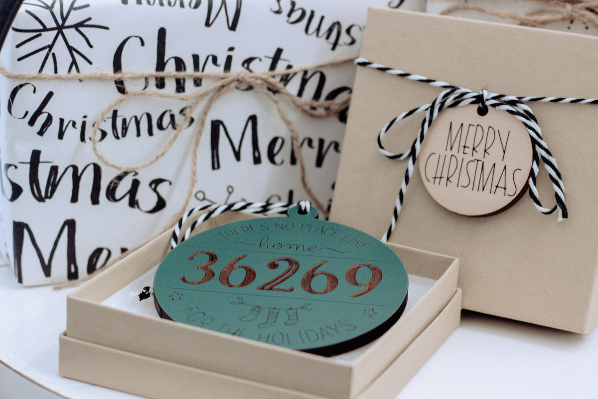 Personalized home holiday ornament set in a box, featuring teal “36269” and gift tags.