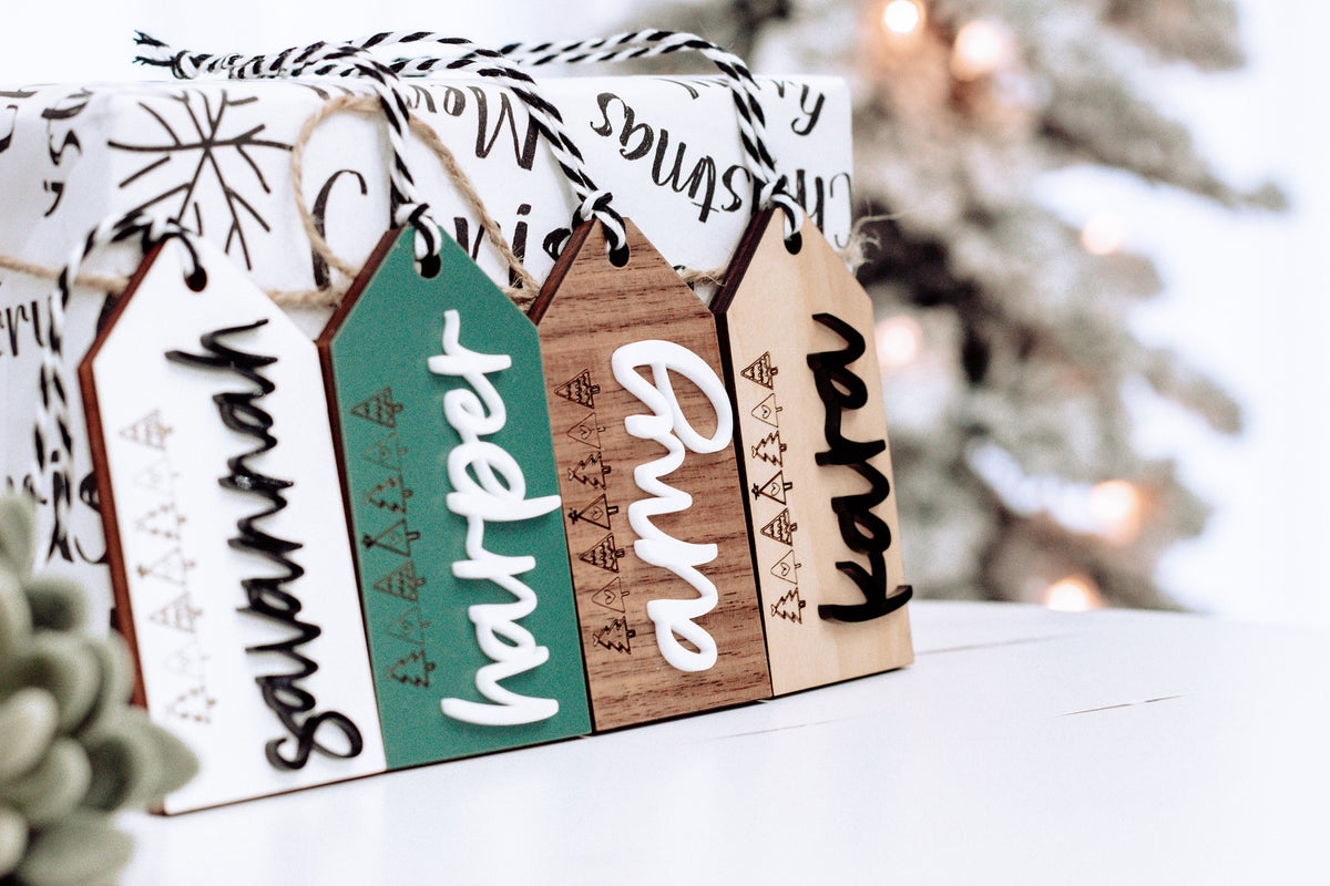 Three personalized stocking gift tags on twine with green and wood name labels.