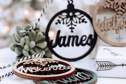 Hanging round name ornament with snowflake design, dark text on a light background