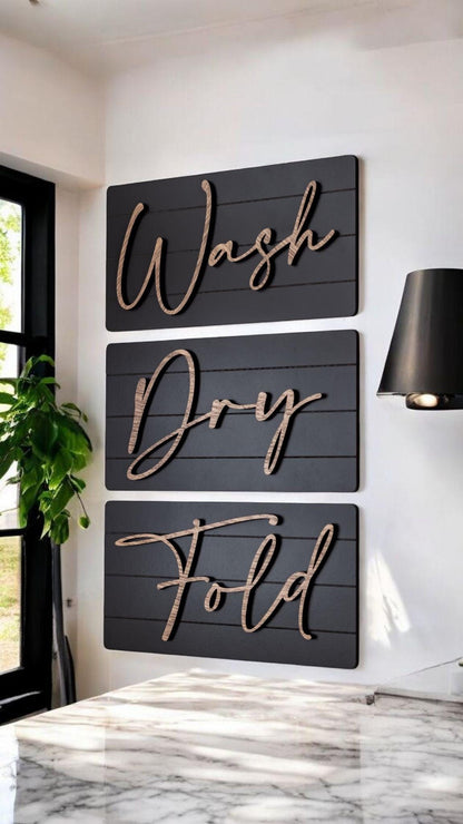 Three dark farmhouse wall signs reading Wash, Dry, Fold with wood-tone cursive lettering