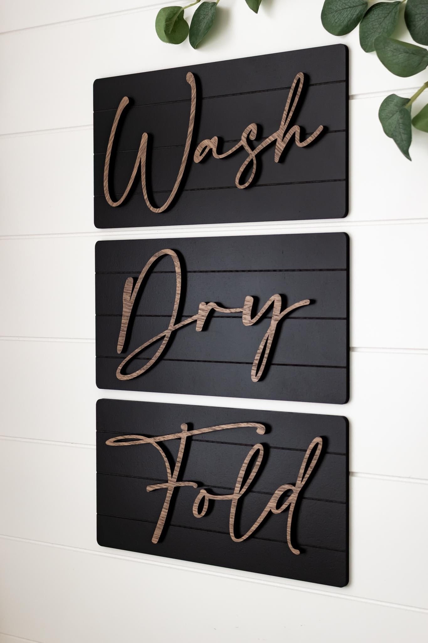 Three dark wall decor signs stacked with cursive words Wash, Dry, Fold