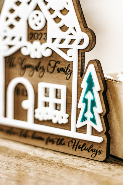 Wood gingerbread house ornament close-up with “2023” and “Gonzalez Family,” teal tree