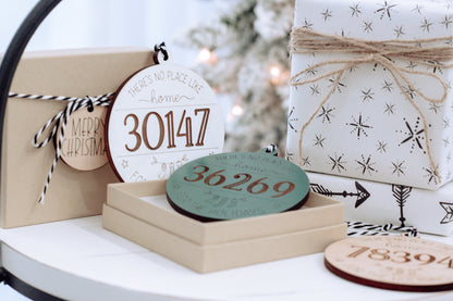 Set of round personalized home holiday ornaments in white and teal with engraved zip codes.
