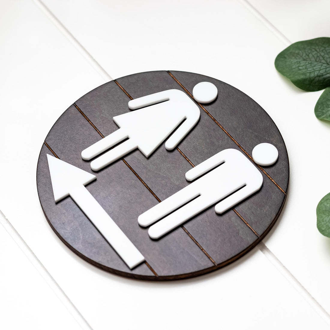 Directional restroom sign with white male and female icons on dark round grid backing