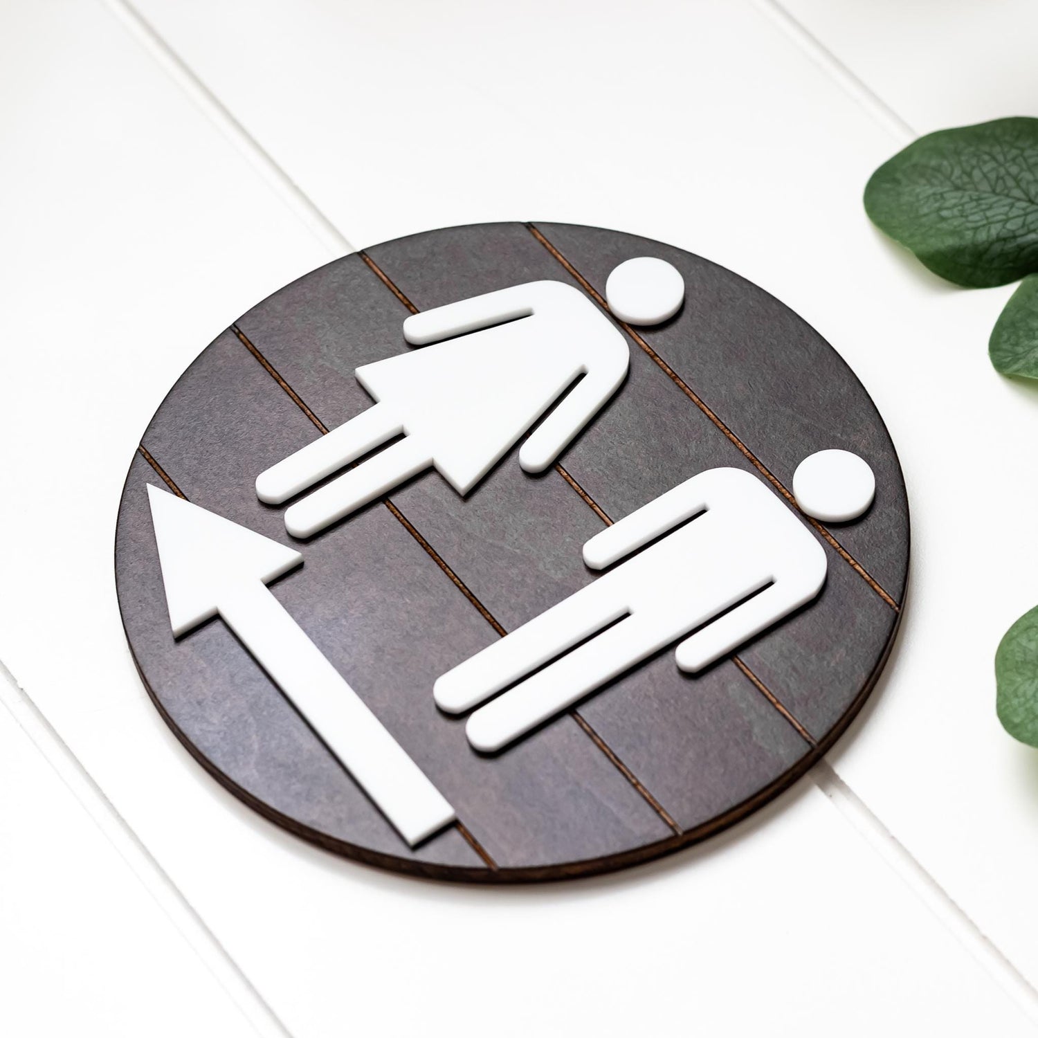 Directional restroom sign with white male and female icons on dark round grid backing