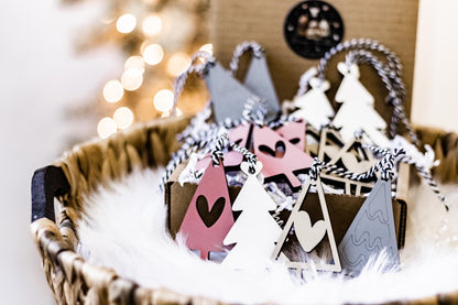 Wooden Christmas ornaments in blush, white, and gray with tree shapes and braided hangers