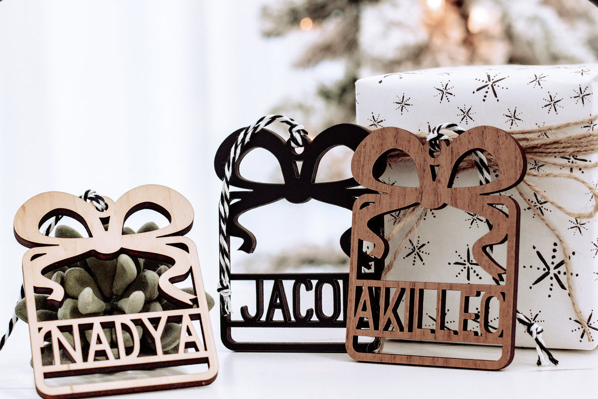Three wooden laser-cut name ornaments in light, black, and walnut tones