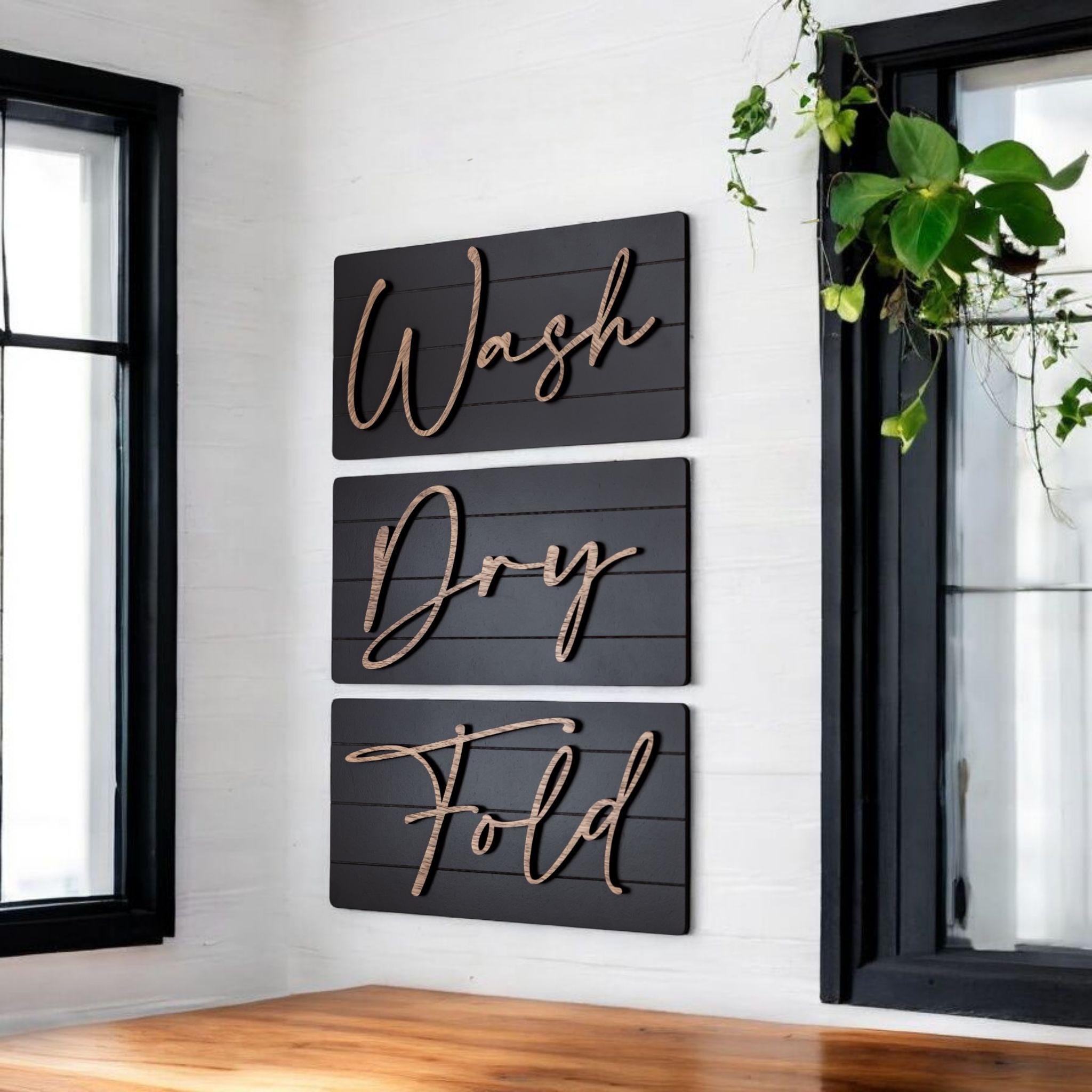 Wall decor sign set with three dark panels reading Wash, Dry, Fold in cursive script