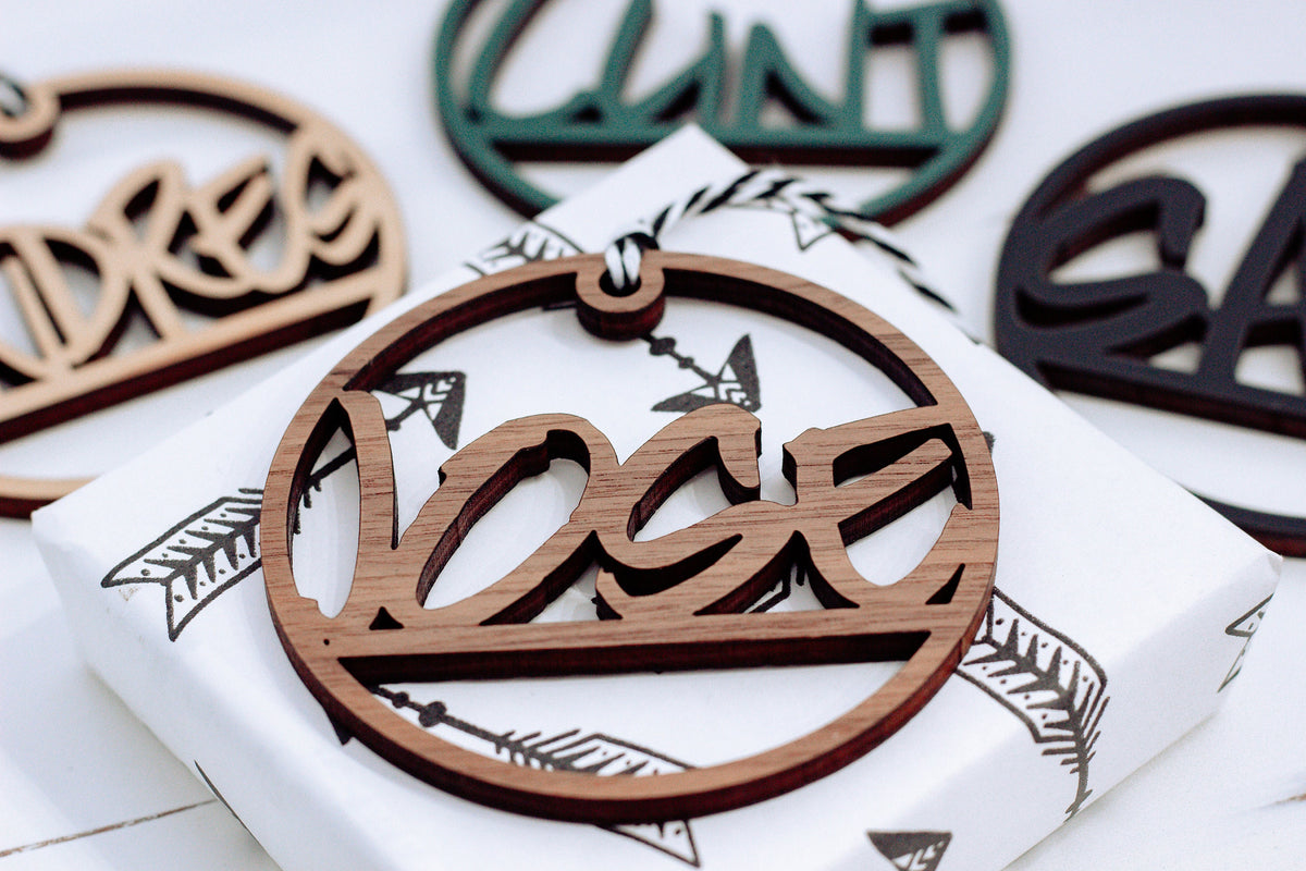 Brown wooden laser-cut custom name ornament with hanging loop and ribbon, round shape