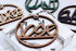Brown wooden laser-cut custom name ornament with hanging loop and ribbon, round shape