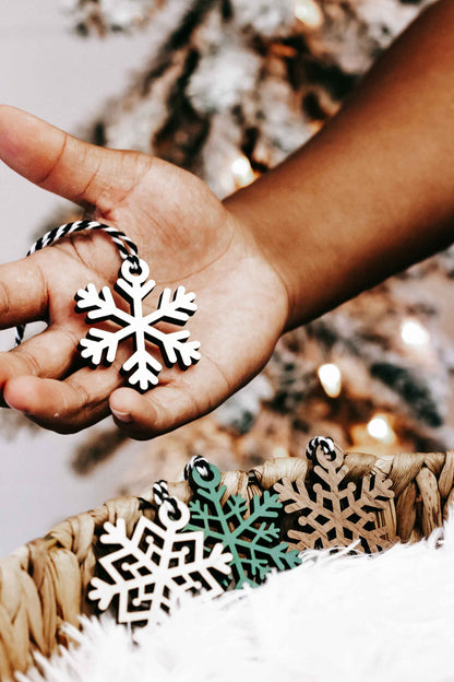 Snowflake wooden ornament held in hand, black and white cutout design with small loop