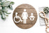 Accessibility restroom sign, round dark plaque with wheelchair and female figure icons