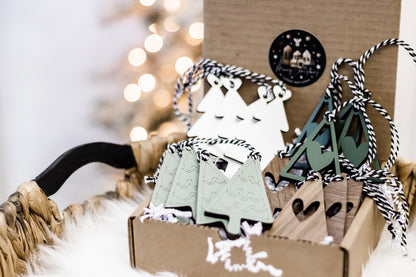 Wood and paper Christmas tree ornaments with striped cords, shown in kraft box