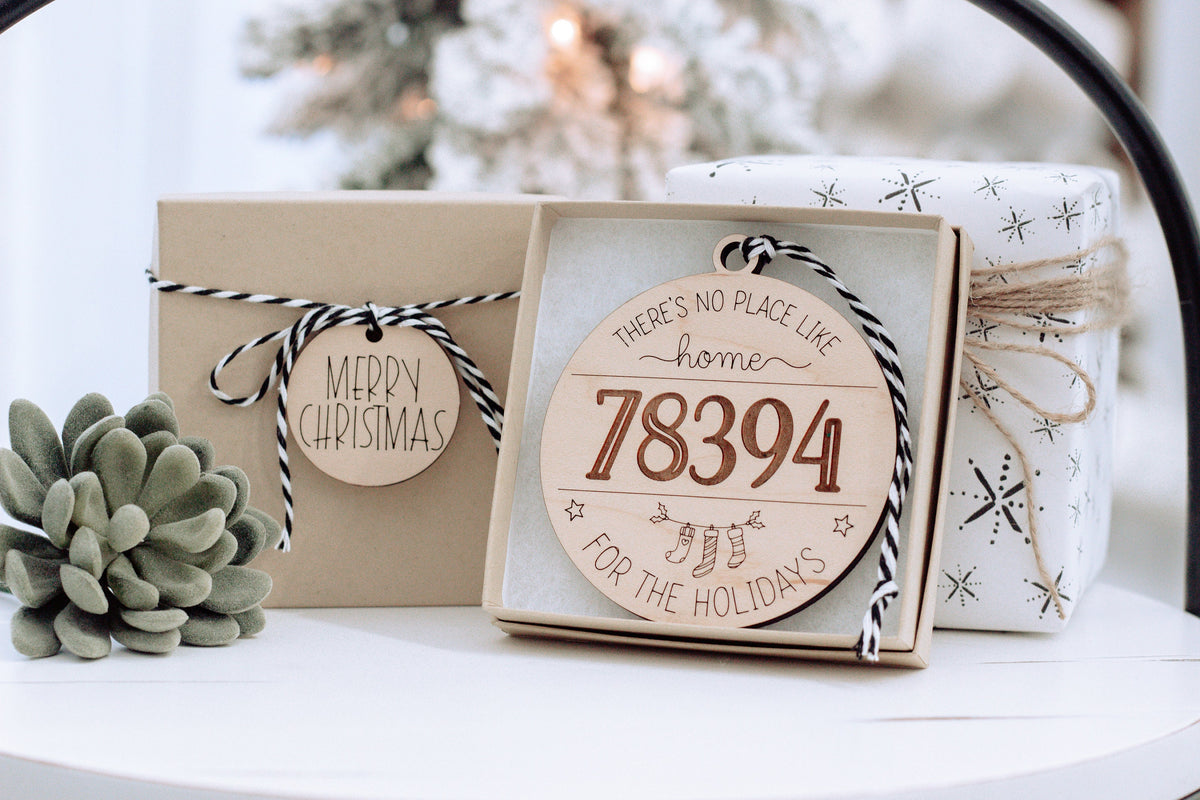 Personalized home holiday ornaments in gift box: white wood “78394” and small “Merry Christmas” tag.