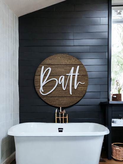 Round wood bath wall sign with white “Bath” lettering on a dark wall