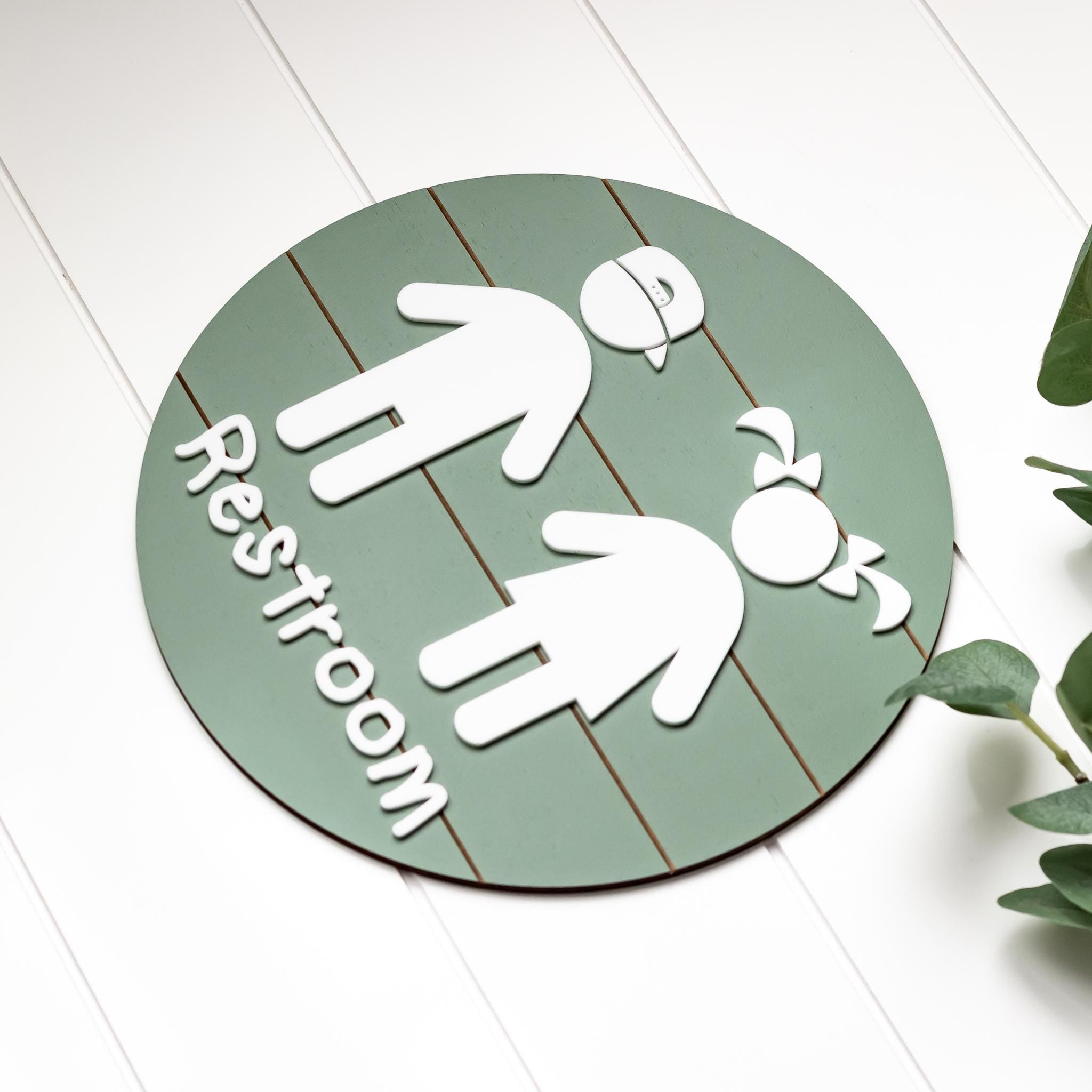 Round green 3D toddler restroom sign with two white child figures and “Restroom”