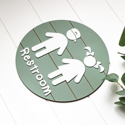 Round green 3D toddler restroom sign with two white child figures and “Restroom”