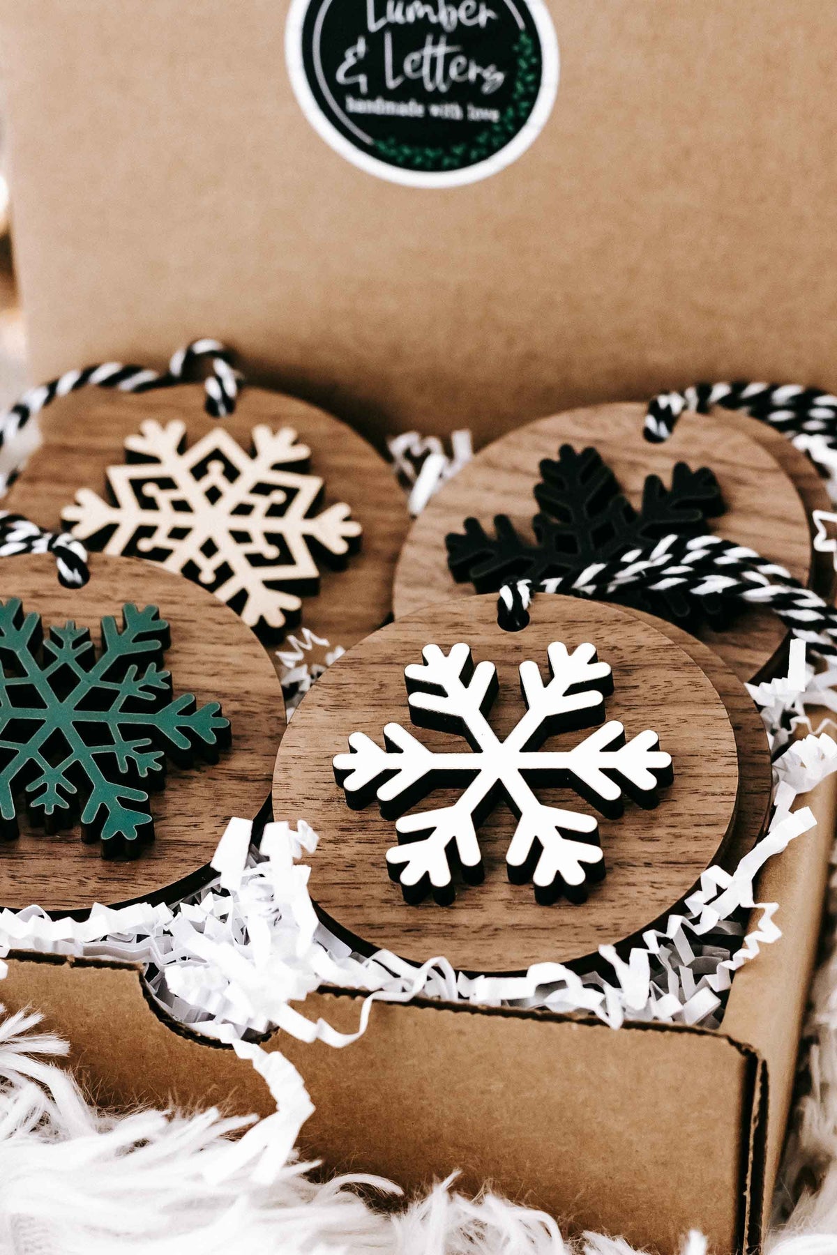 Box set of wooden snowflake ornaments with striped hangers in white, green, and black